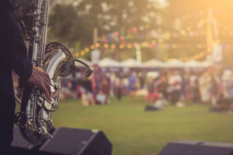 from behind the stage, someone plays the saxophone as a crowd of people at the concert sit in the background