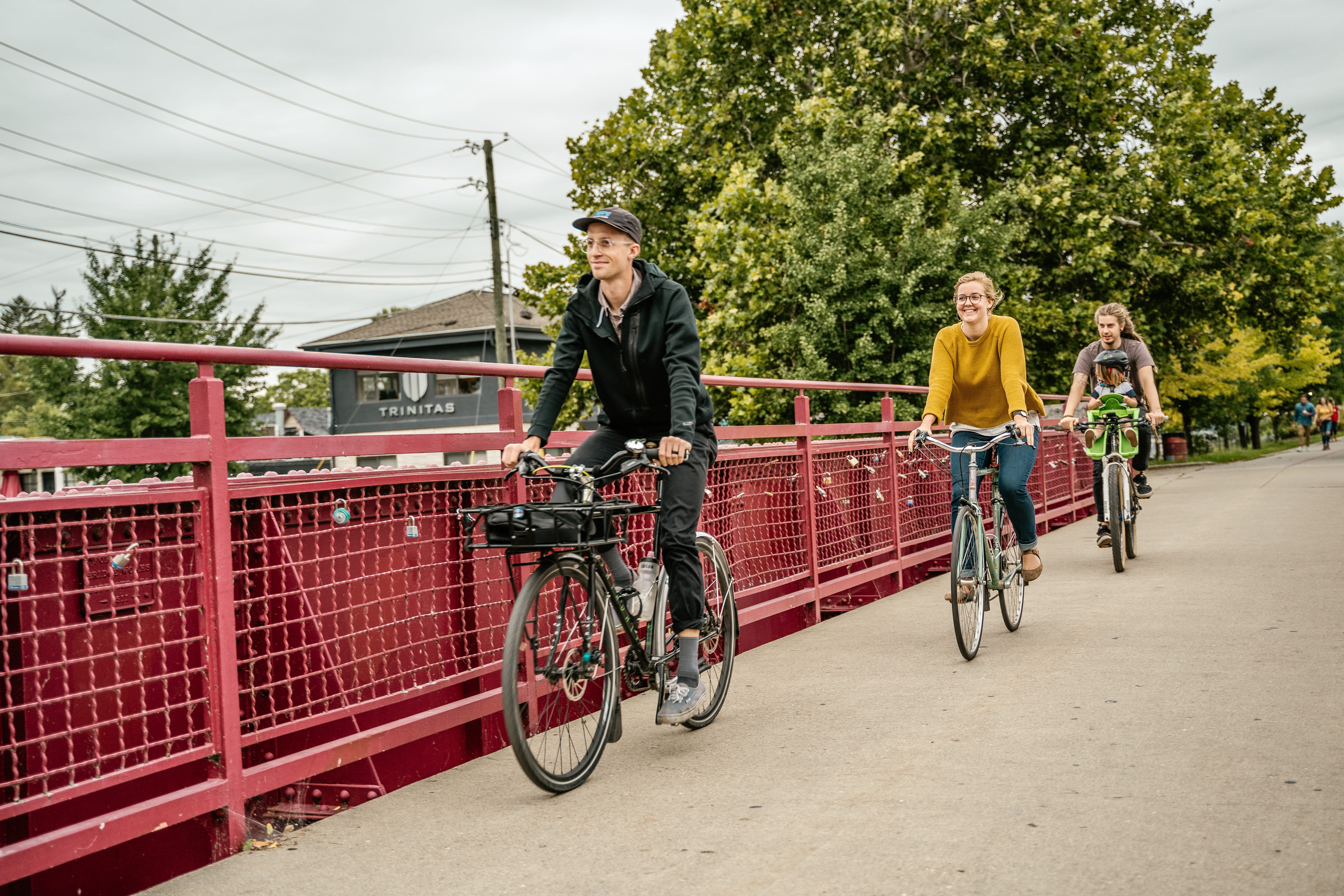 three people ride bikes across a red metal bridge
