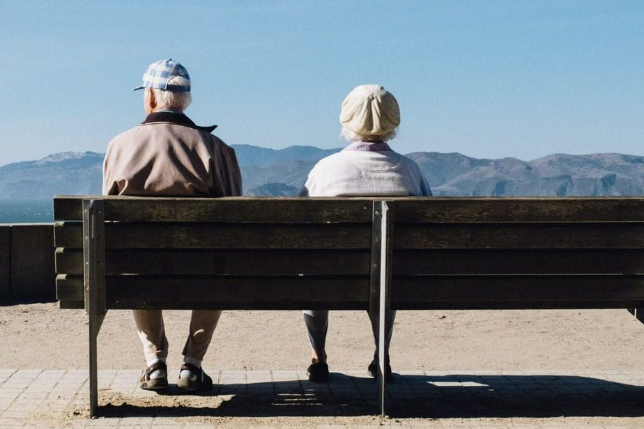 two elderly people sit together on a bench looking at a beautiful view
