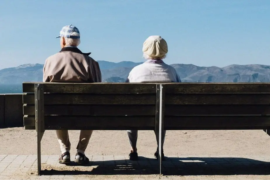 two elderly people sit together on a bench looking at a beautiful view