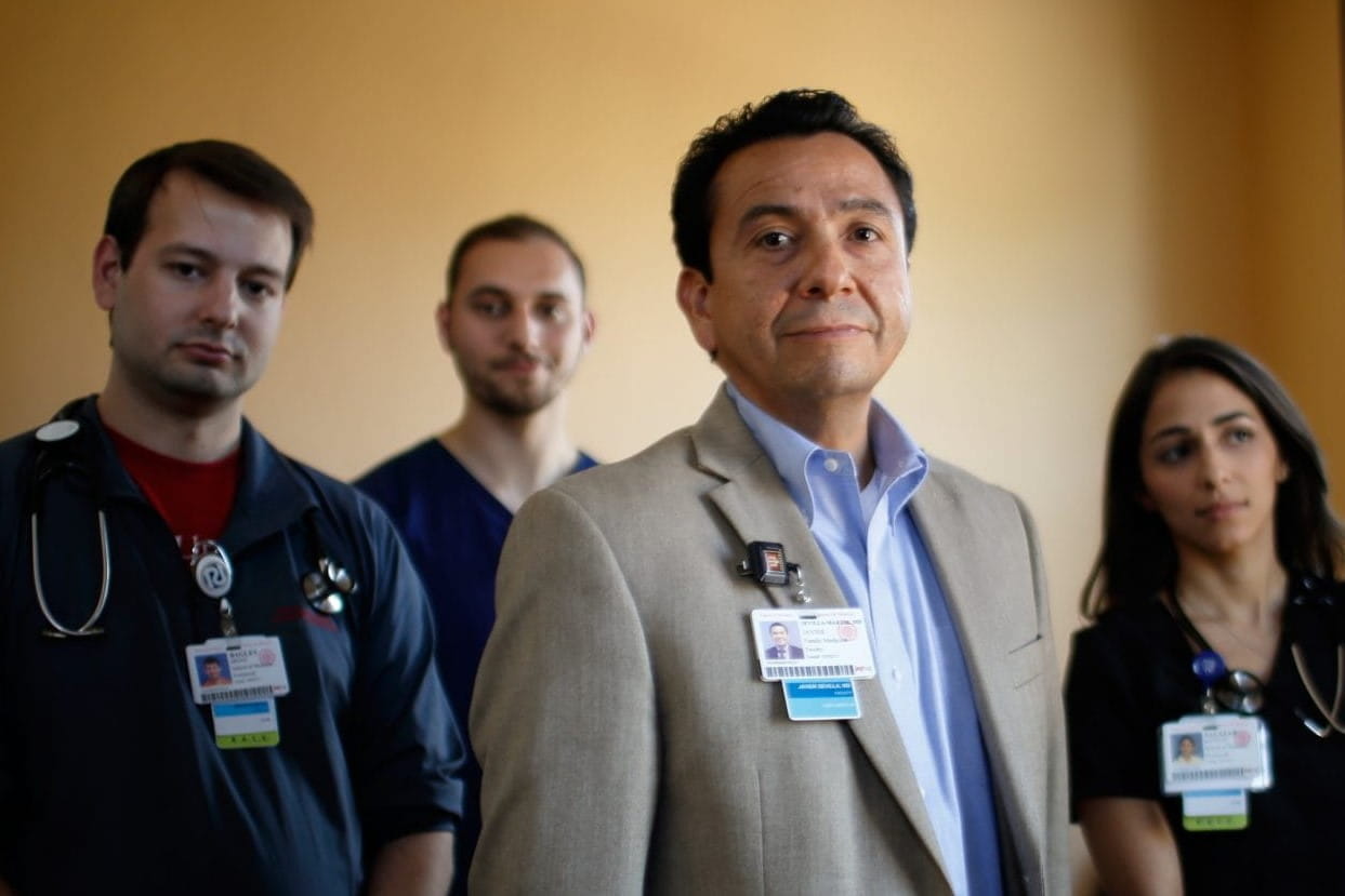 a faculty member stands in front of a group of medical students looking confidently at the camera