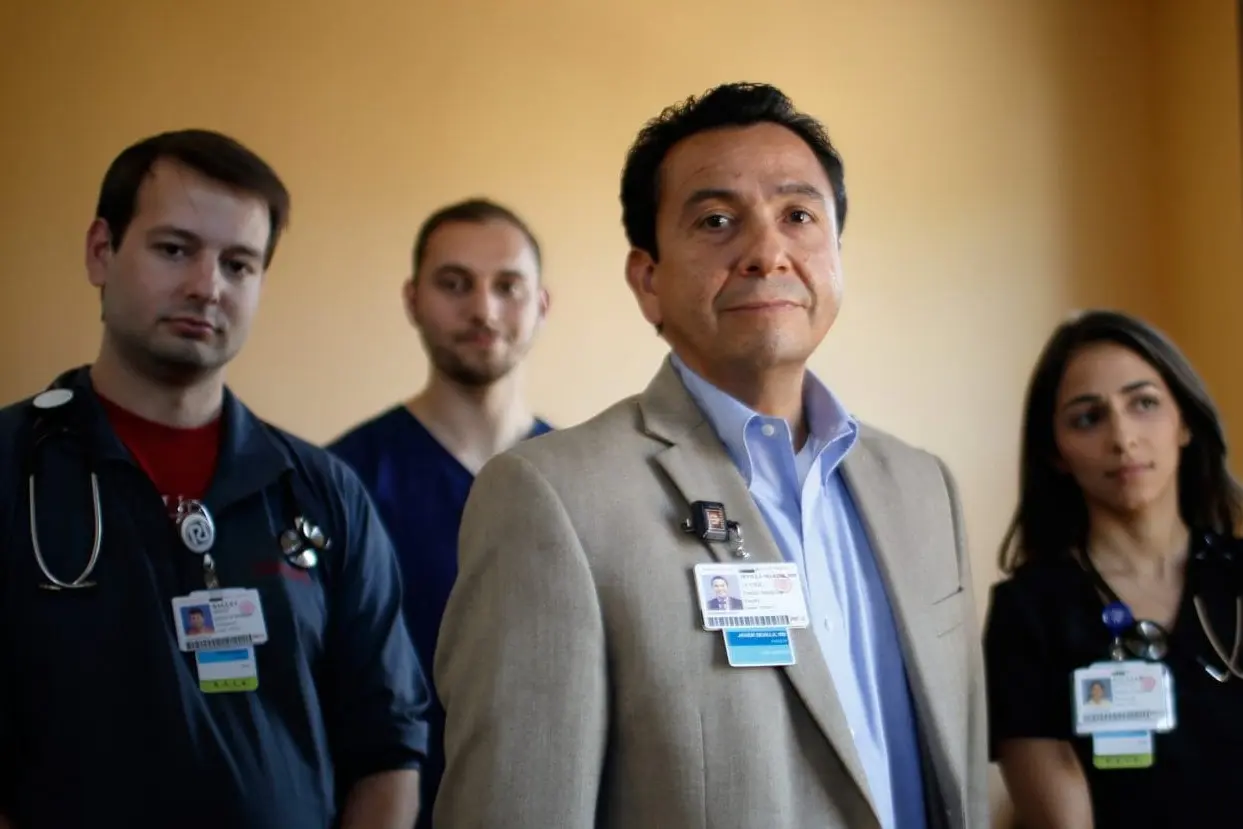 a faculty member stands in front of a group of medical students looking confidently at the camera