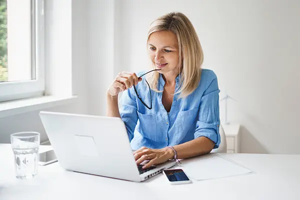 A satisfied woman is looking at a laptop and holding eyeglasses
