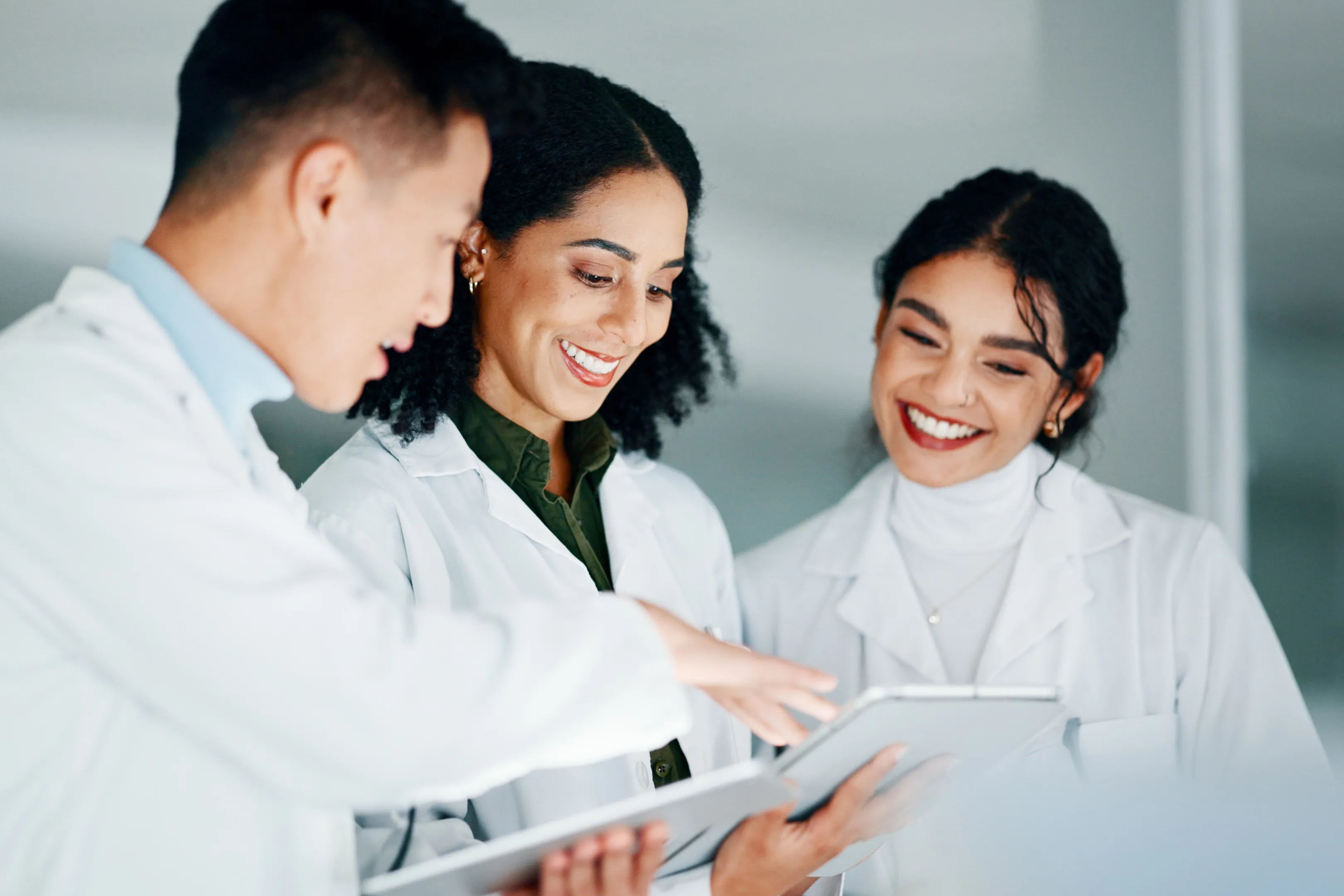 Three researchers in white lab coats are looking at a digital tablet and discussing what they see.