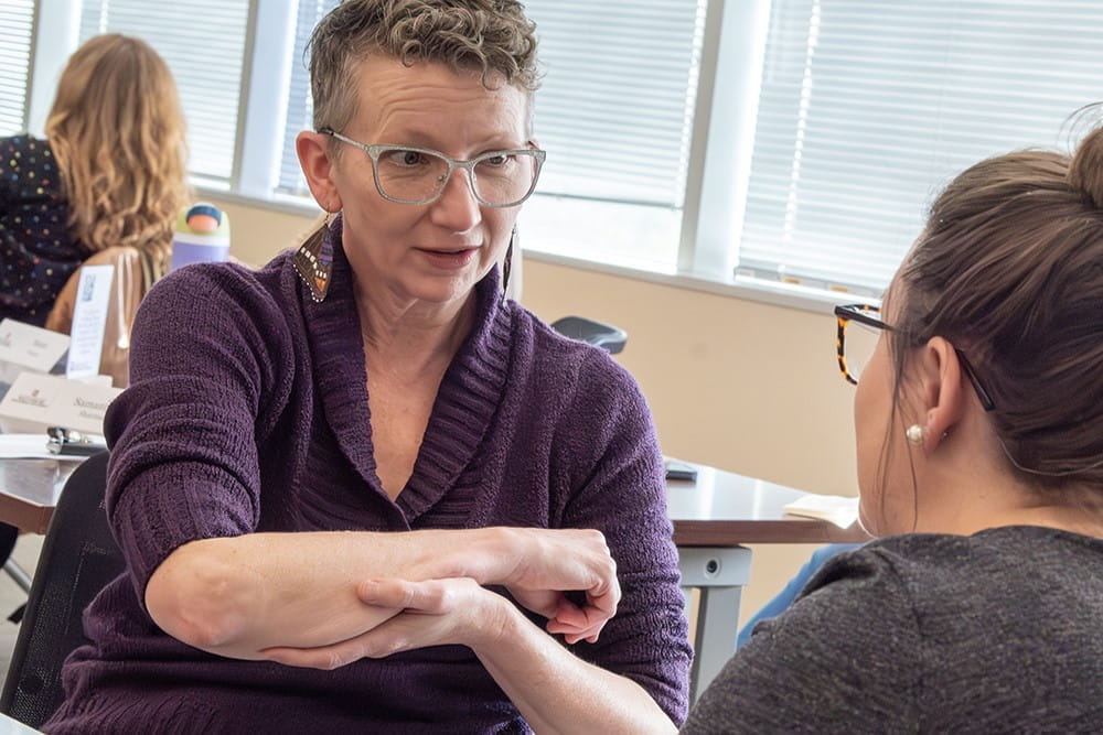 During an improv exercise called "Time Traveler," Kate Kollman, NP, a 2025 Communicating Science participant, attempts to explain — to a scene partner who plays the part of a person who lived more than a century ago — how X-ray technology allows someone to "see" a broken bone.