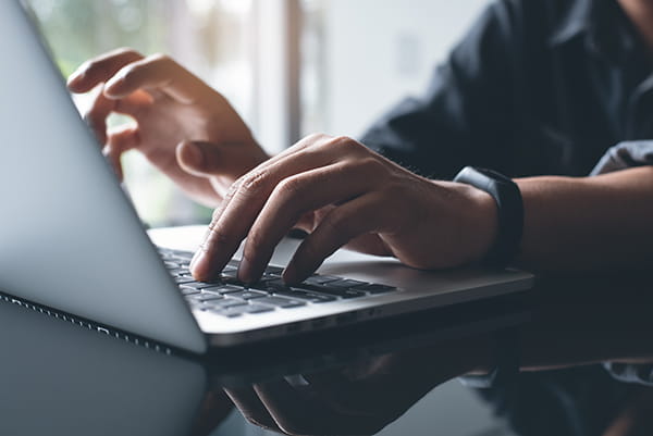 A close-up photo of man's hands as he types on a laptop