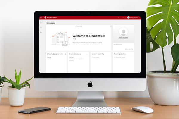 A mock-up of a desktop computer with the home page of Elements loaded on the screen. The computer is surrounded by two potted plants.
