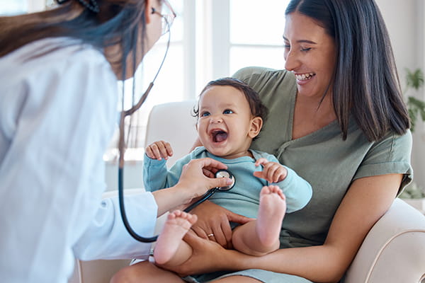 A medical student holds her child while the baby is examined by a healthcare provider.