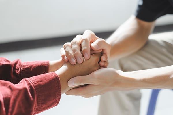 Two people hold hands in support of one person's difficult time