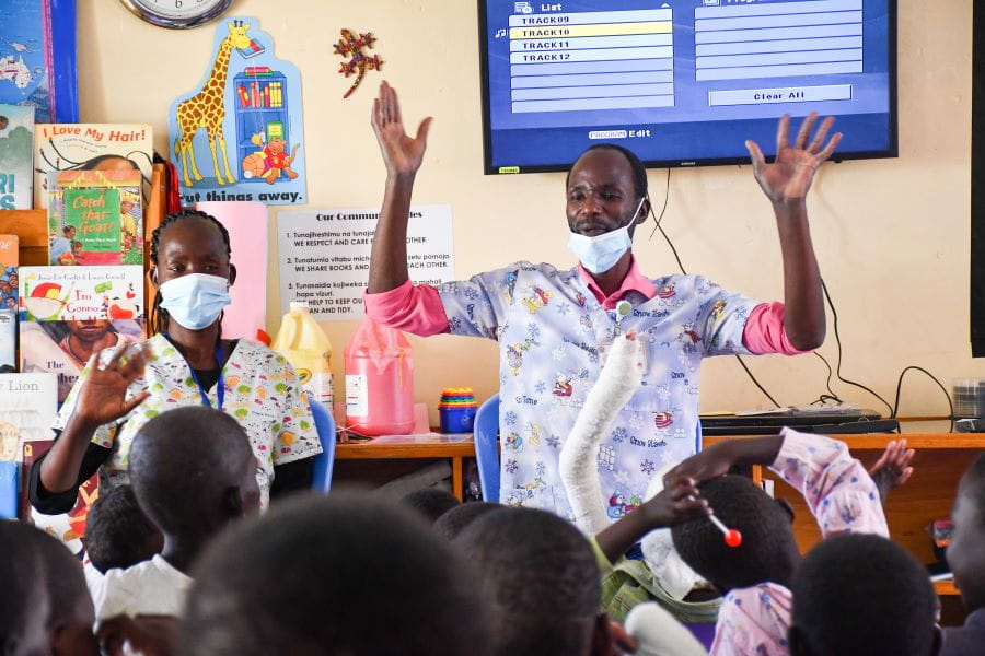 two health care workers lead a game in front of a room of children on valentines day at the sally test center