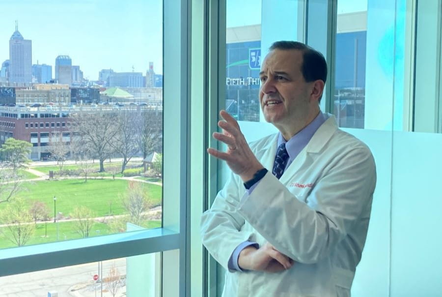 Photo of David M. Haas, gesturing with his left hand as he's speaking by a window, showing the skyline of downtown Indianapolis.