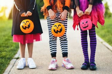 kids with Halloween costumes on and jack-o-lantern buckets to collect candy