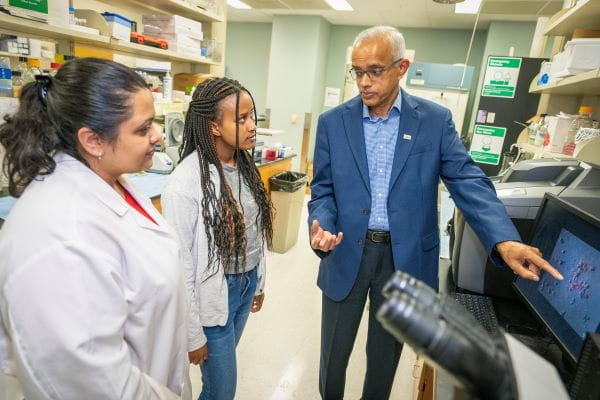 Harikrishna Nakshatri works with two students in the lab, pointing to a screen and speaking.