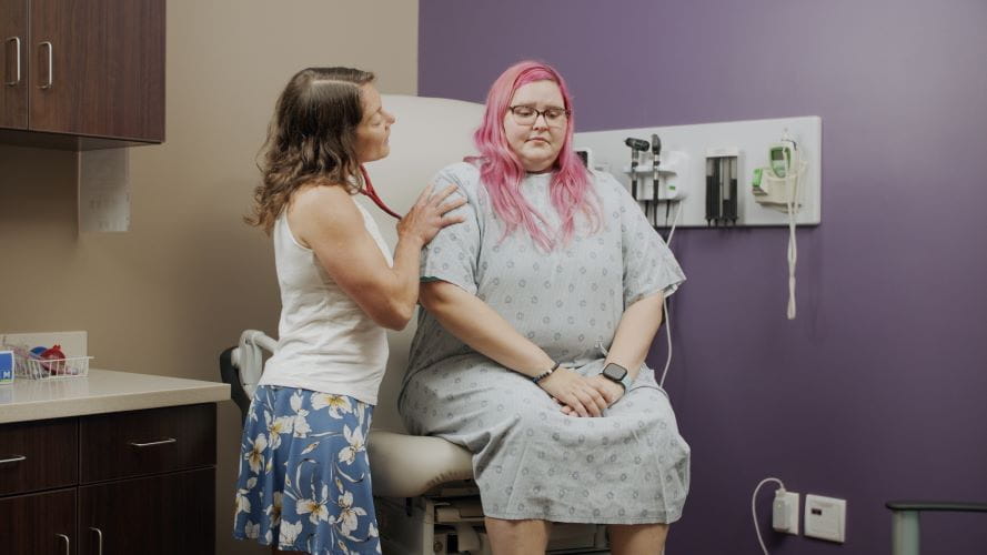 female doctor listening to back of female patient