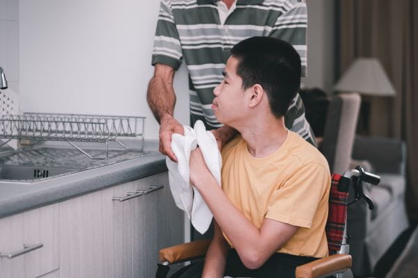 a person dries their hands on a towel with assistance from a caregiver