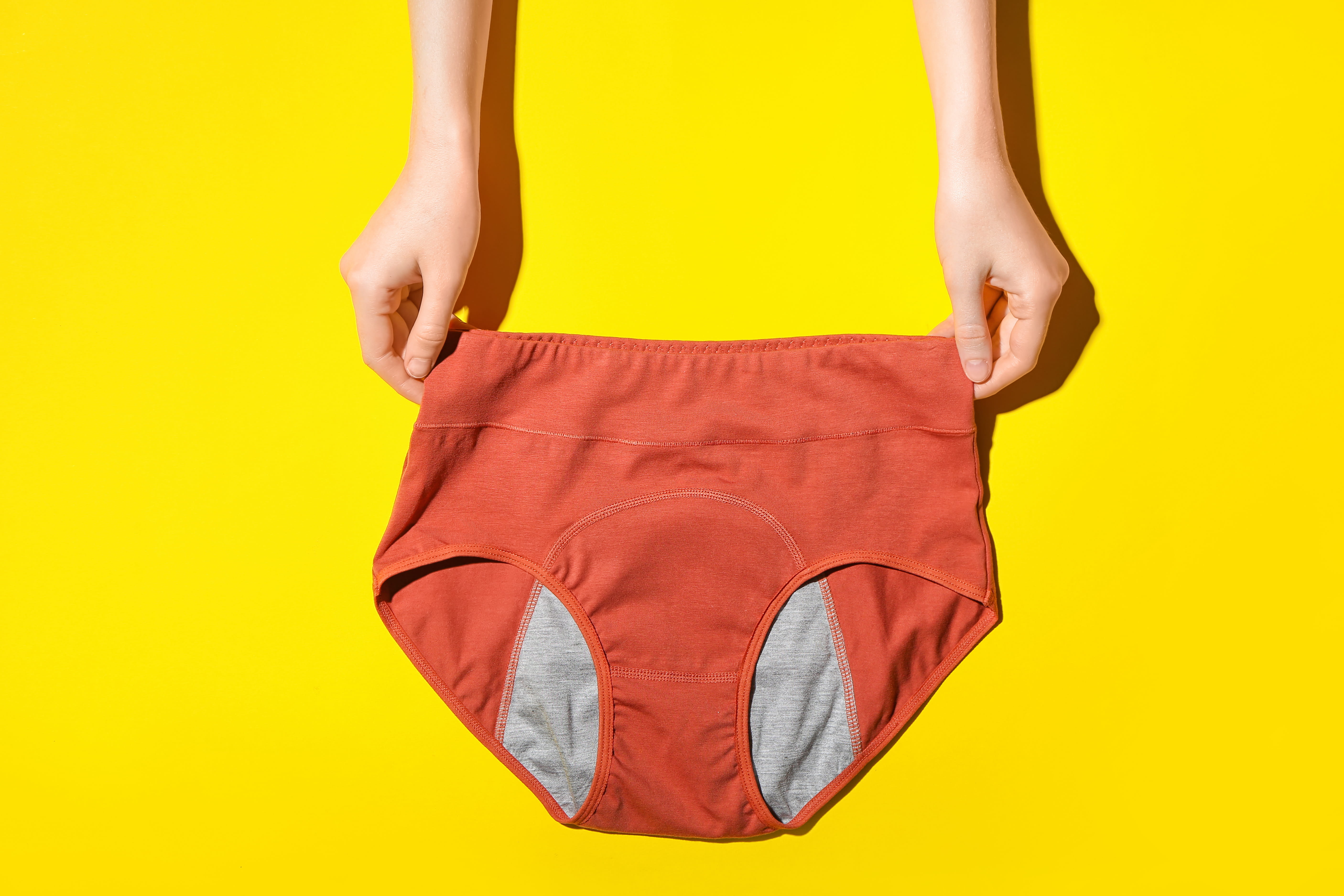 two hands holding orange period panties