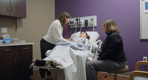 female doctor examining the belly of a female patient and female caretaker