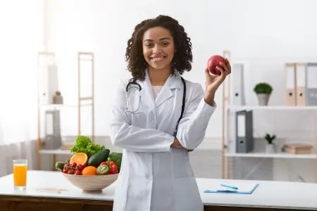 african american female dietician holding a piece of fruit in a kitchen
