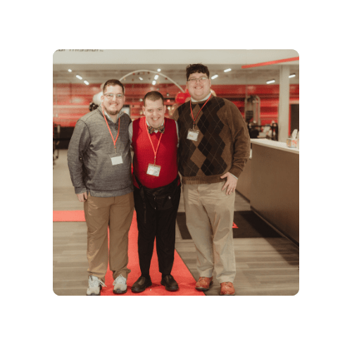 3 brothers, 1 with an intellectual disability, standing on a red carpet,