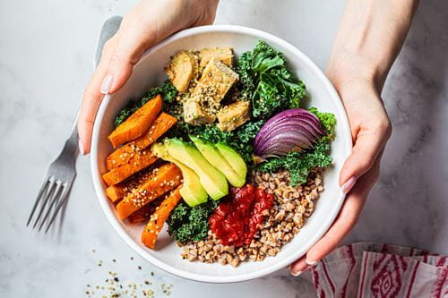 bowl of sweet potatoes, leafy greens, grains, avocado and onion