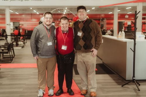 3 brothers, 1 with an intellectual disability, standing on a red carpet,