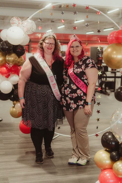 two women with disabilities standing in front of a photo backdrop smiling