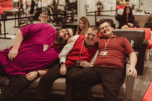three men with disabilities sitting on a couch together smiling 