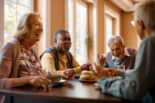 one female and 3 male elderly friends sitting around a table talking