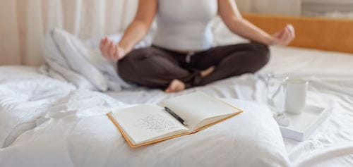 person meditating and a journal laid out on bed