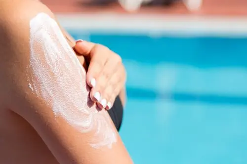 person applying sunscreen in front of a pool