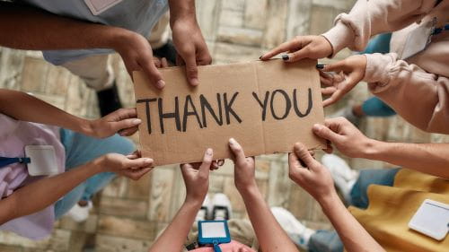 several hands holding a piece of cardboard that says thank you