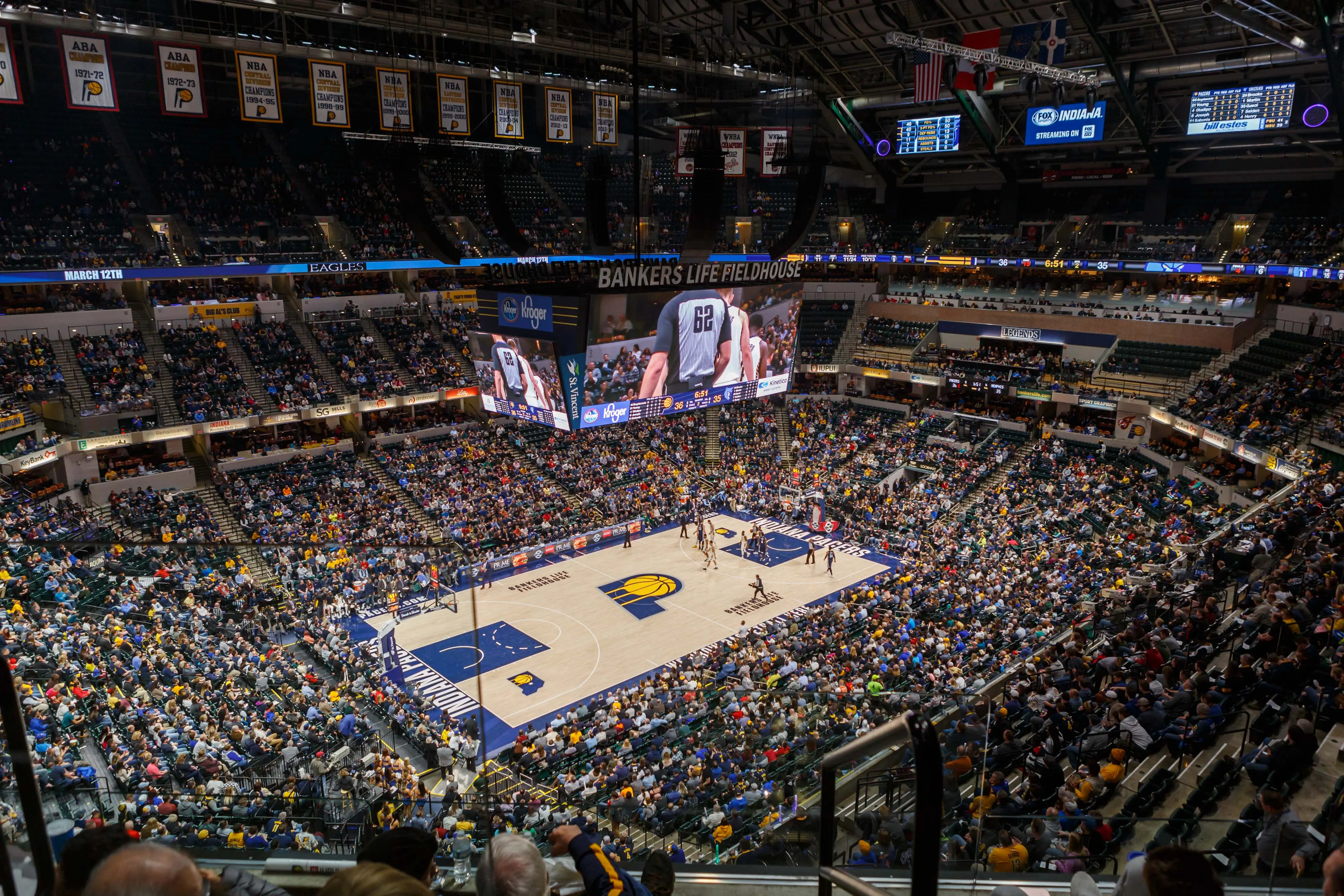 Wide view of a basketball game at Gainbridge Fieldhouse in Indianapolis, with a packed crowd and the Indiana Pacers court visible below a large center scoreboard.