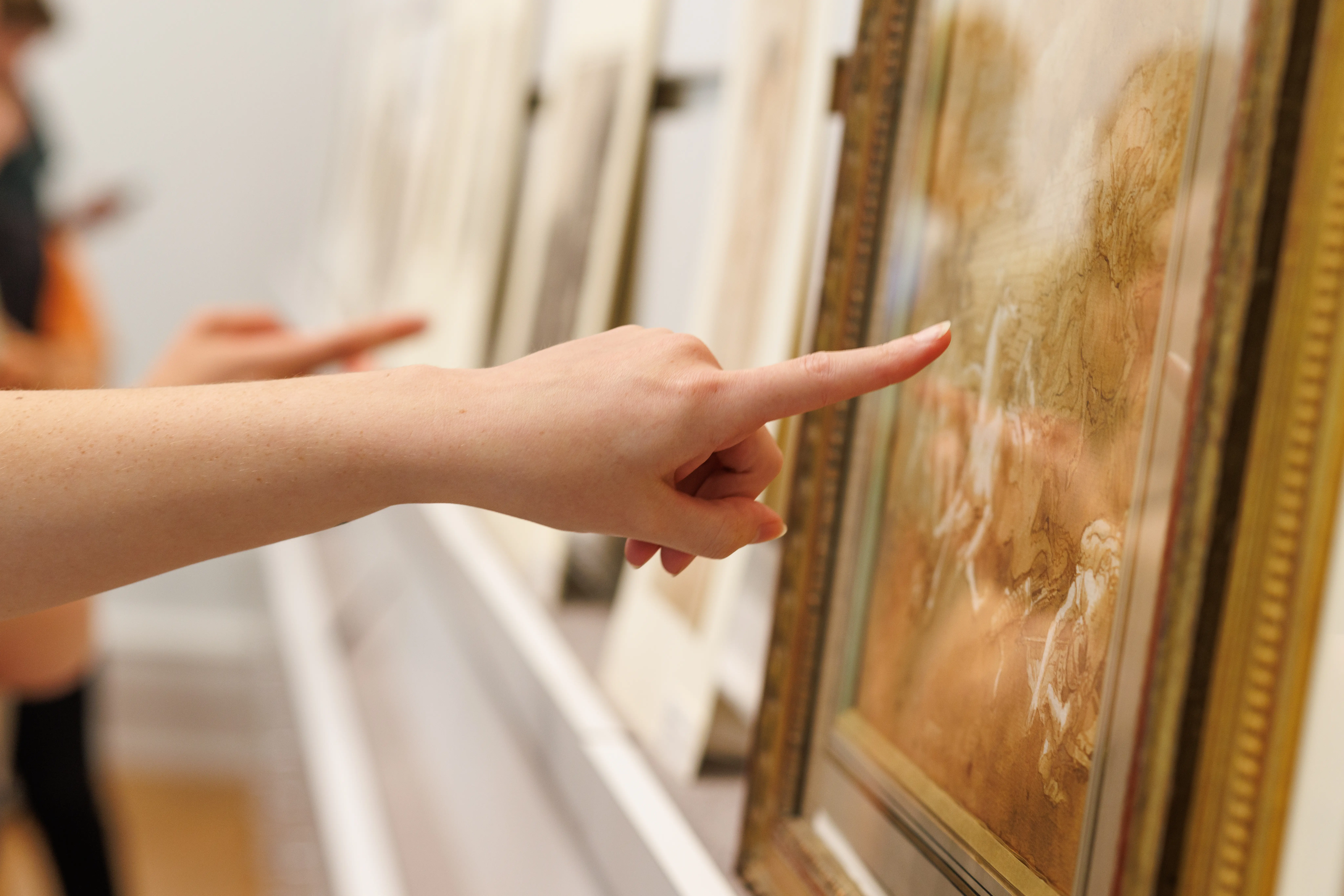 Close-up of a person pointing at framed artwork in a museum or gallery setting.