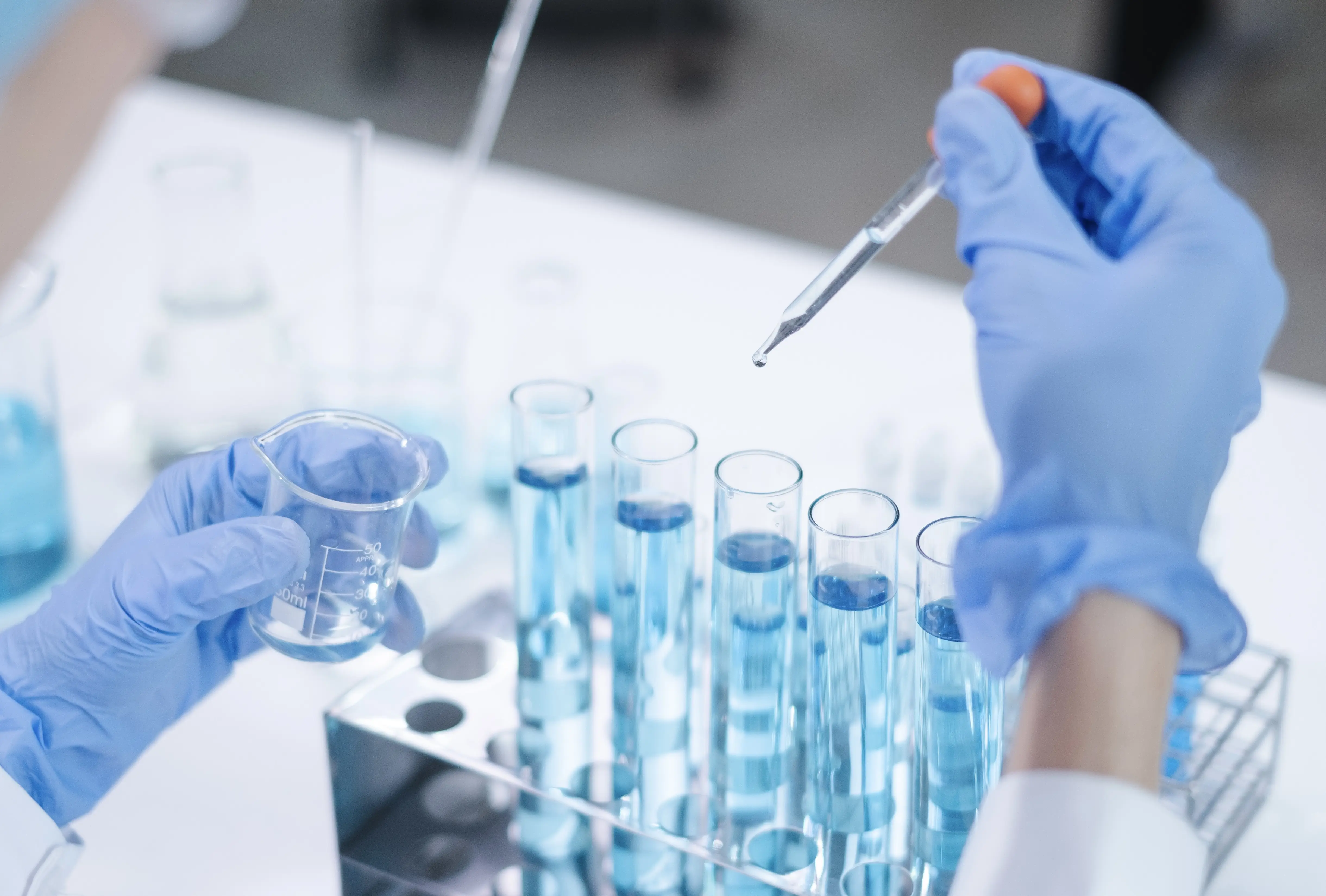 doctor in lab with blue gloves on and a dropper in hand placing liquid into viles