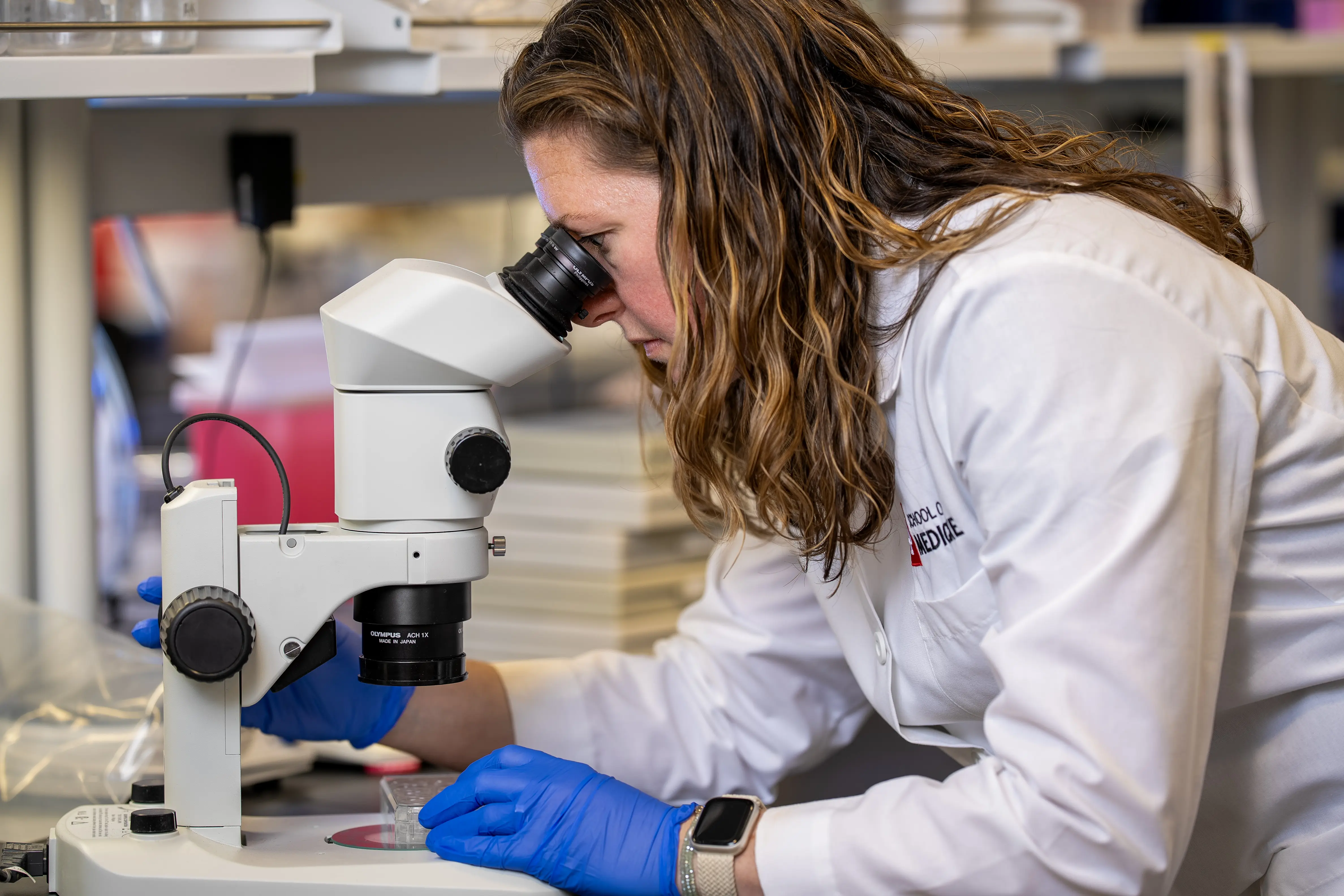 A woman in a lab coat looks into a microscope
