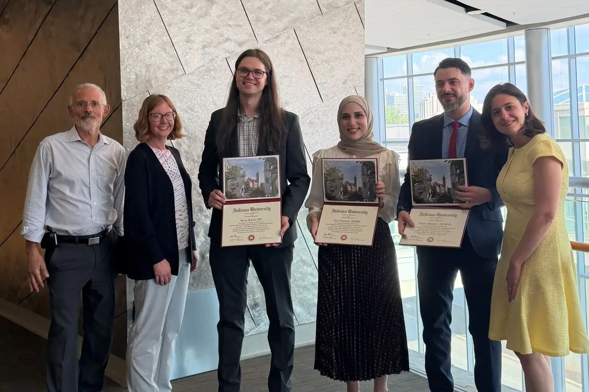 Six smiling people pose in well lit atrium; three people are holding graduation certificates.