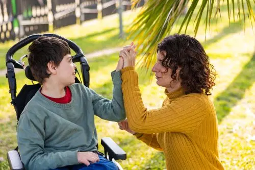 Mother playing with son with disability in wheelchair outdoors