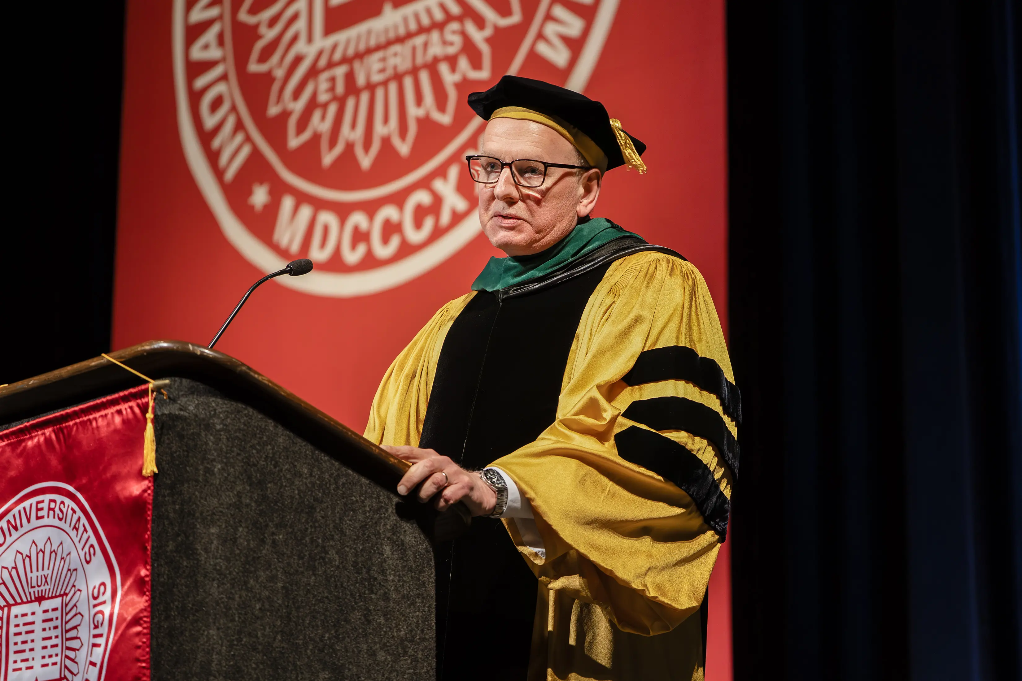 A doctor in robes speaks at a podium, 