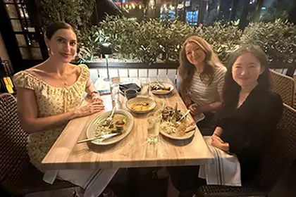Three people seated around a wooden table at an outdoor restaurant patio in the evening.