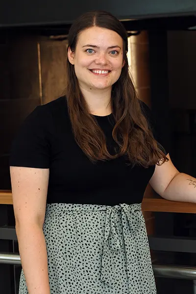 Portrait of a person standing indoors beside a metal-and-wood railing in a modern building.