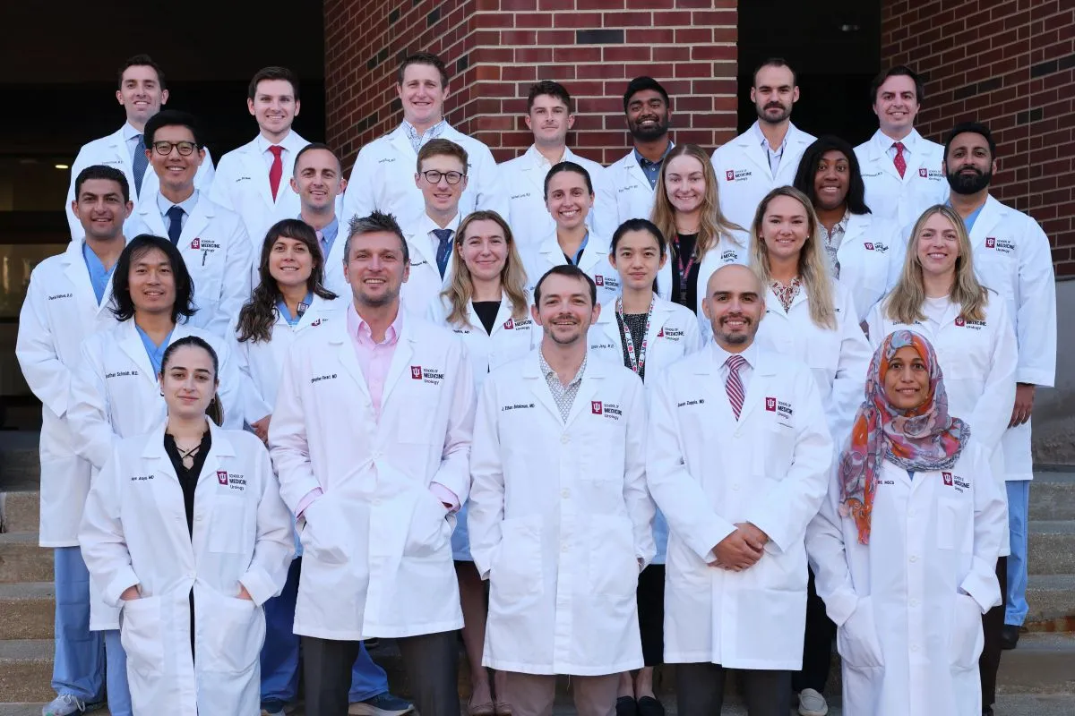 Group photo of the Indiana University School of Medicine Department of Urology residents and faculty standing together outside the department building in white lab coats.