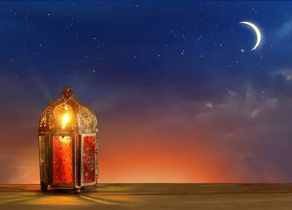 Illustration of a lit lantern on a wooden surface, against a sunset with a crescent moon in the upper right hand corner