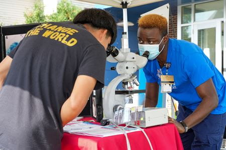 Adeyinka Akinsanya chats with the teenager standing opposite him and explaining slides he’d slipped under a microscope setup between them.