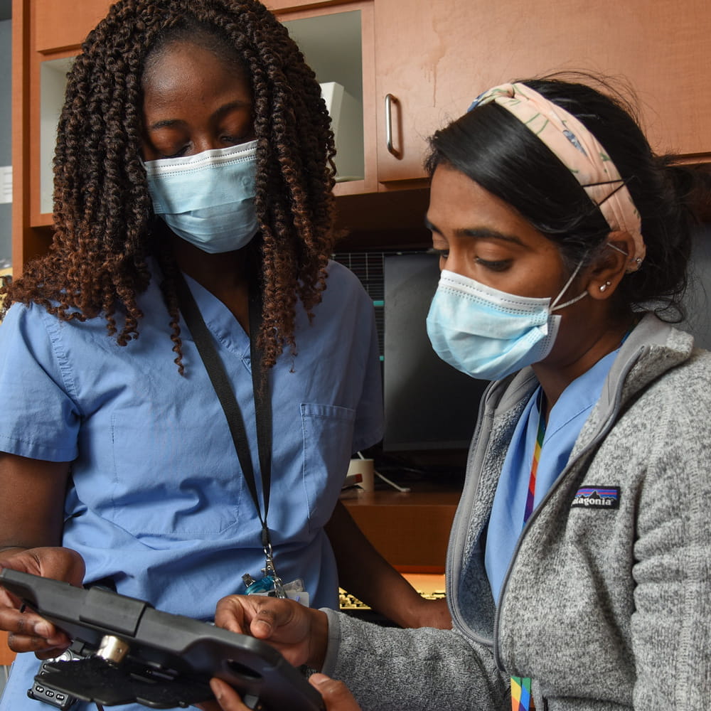 two residents look at patient information together in a work room