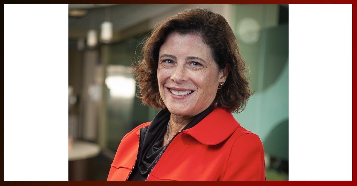 Dr. LaMothe stands in front of a nondescript background wearing a red, collared jacket over a black top. She is smiling at the camera. 
