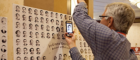 an older white man uses his phone to take a picture of an alumni photo composite