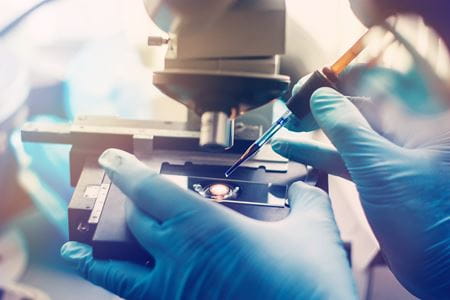 gloved hands prepare a sample under a microscope