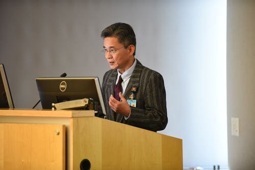 Chi Wah “Rudy” Yung, MD, speaks at a podium in a lecture hall in the Glick Eye Institute.