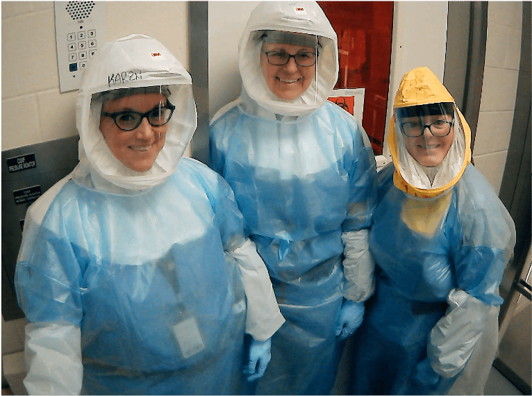 Melissa Kacena poses with two other researchers. All three people are smiling and wearing protective coverall suits.