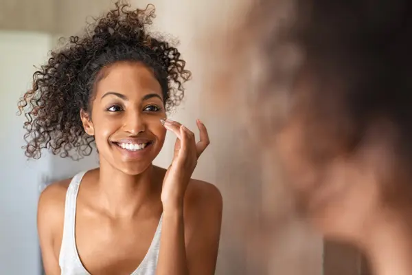 a young black woman applies sunscreen to her face